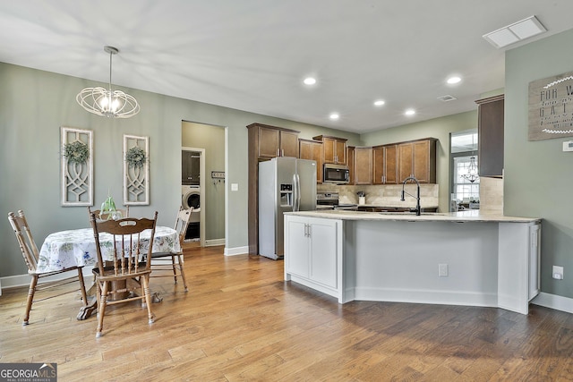 kitchen with backsplash, washer / dryer, appliances with stainless steel finishes, light wood-style floors, and a sink