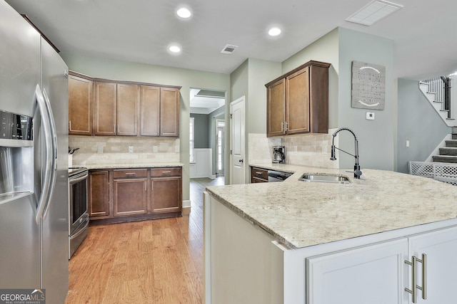 kitchen featuring visible vents, a peninsula, a sink, stainless steel appliances, and light wood-style floors