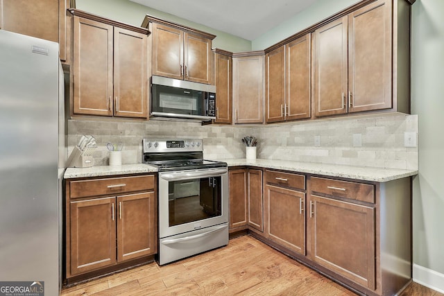 kitchen with light wood-style flooring, light stone counters, tasteful backsplash, and appliances with stainless steel finishes