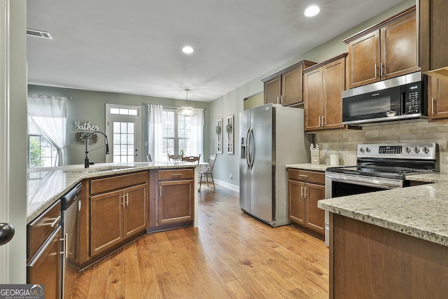 kitchen with light stone countertops, light wood-style flooring, a sink, stainless steel appliances, and backsplash