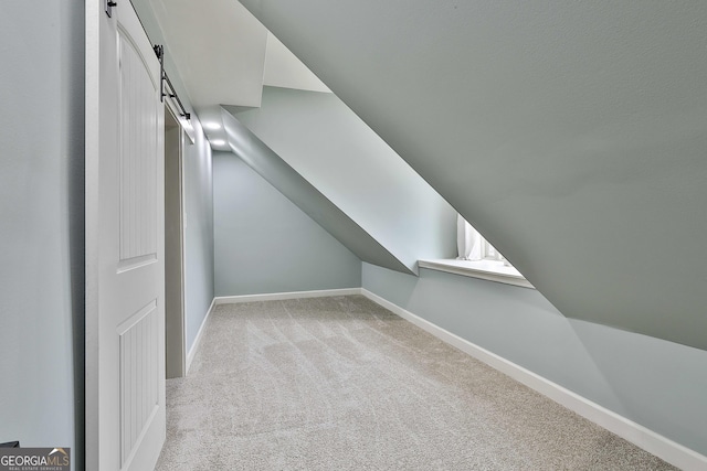 bonus room featuring a barn door, light colored carpet, baseboards, and vaulted ceiling