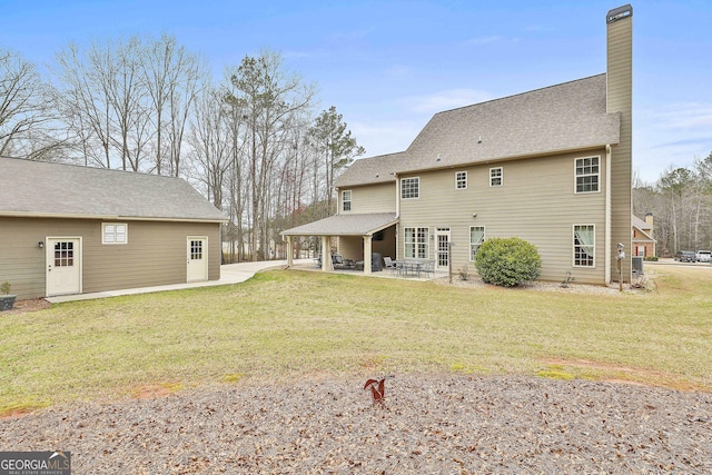 back of property with a patio, a lawn, and a chimney