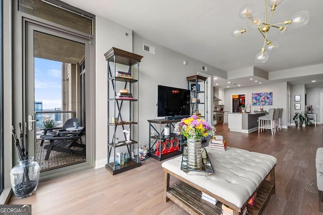 living room with baseboards, a notable chandelier, visible vents, and wood finished floors