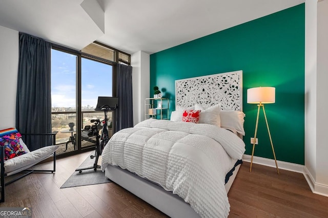 bedroom with an accent wall, expansive windows, baseboards, and wood finished floors