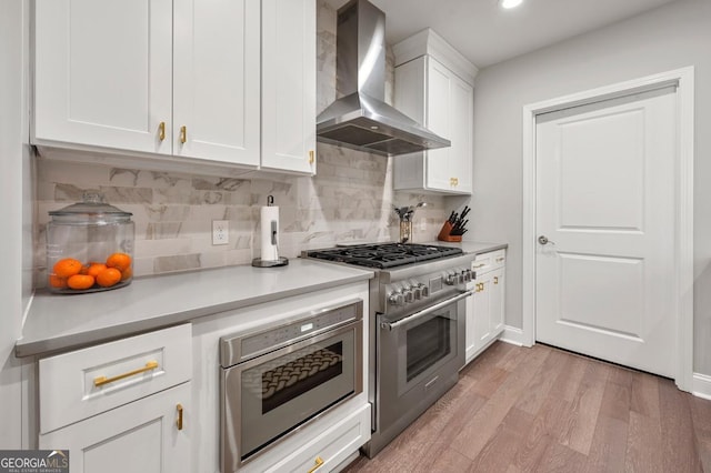 kitchen featuring light wood-style flooring, stainless steel appliances, white cabinetry, light countertops, and wall chimney range hood