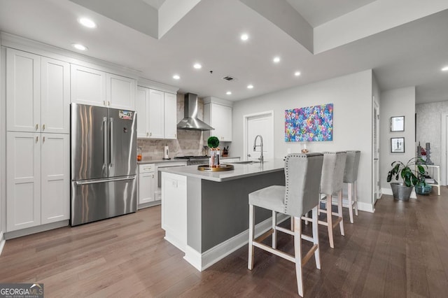 kitchen with high end fridge, white cabinets, a sink, light wood-type flooring, and wall chimney exhaust hood