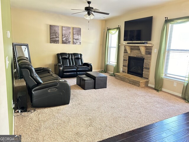 living area featuring a stone fireplace, a healthy amount of sunlight, baseboards, and a ceiling fan