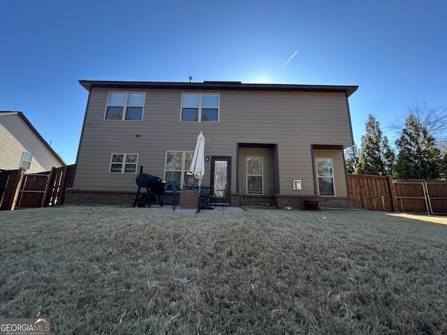 rear view of property with a patio, brick siding, fence, a lawn, and a gate