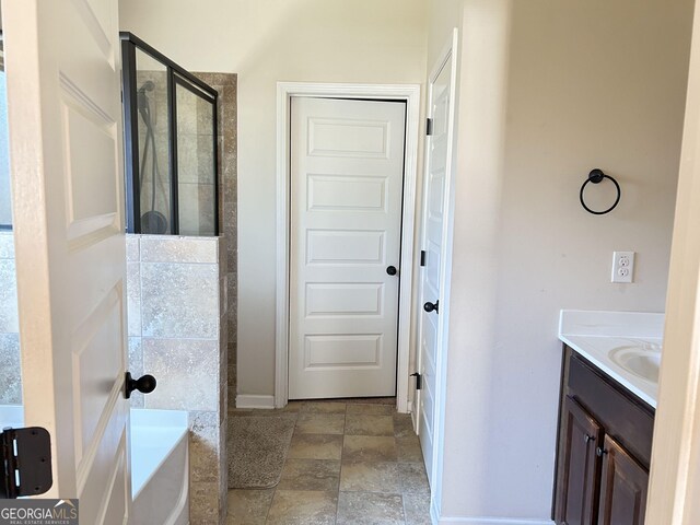 bathroom featuring a shower stall, stone finish flooring, baseboards, vanity, and a garden tub