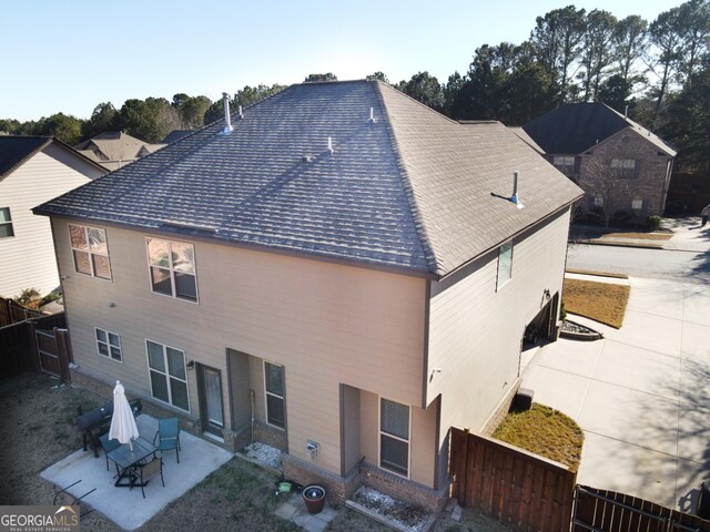 back of house with fence, roof with shingles, and a patio area