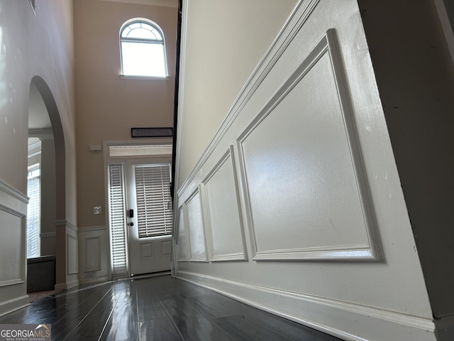 entryway featuring arched walkways, a decorative wall, dark wood-type flooring, a towering ceiling, and wainscoting