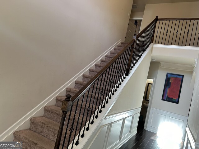 stairs featuring a wainscoted wall, a decorative wall, baseboards, wood finished floors, and a high ceiling