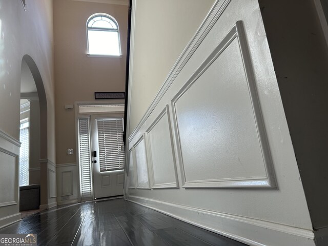 entrance foyer featuring dark wood finished floors, wainscoting, a decorative wall, arched walkways, and a towering ceiling