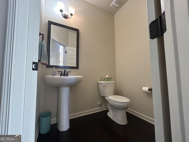 half bath with toilet, visible vents, baseboards, and a sink