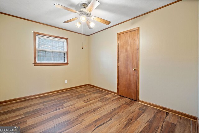 spare room with a ceiling fan, crown molding, baseboards, and wood finished floors