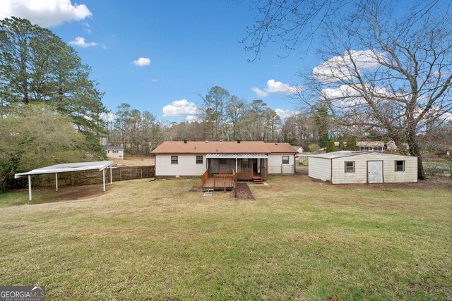 rear view of property featuring fence, an outdoor structure, a lawn, and a detached carport