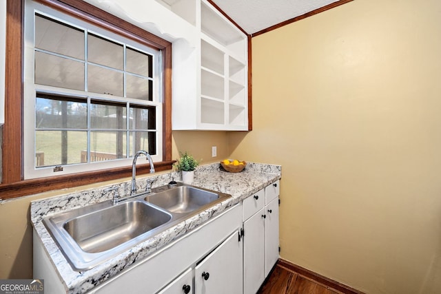 kitchen with dark wood-style floors, white cabinetry, a sink, and baseboards