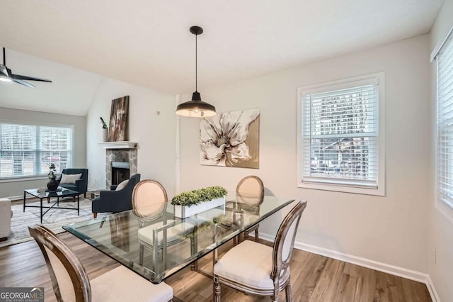 dining space with a stone fireplace, wood finished floors, a ceiling fan, and baseboards