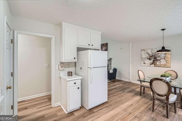 kitchen with light countertops, light wood-style floors, freestanding refrigerator, white cabinets, and a textured ceiling