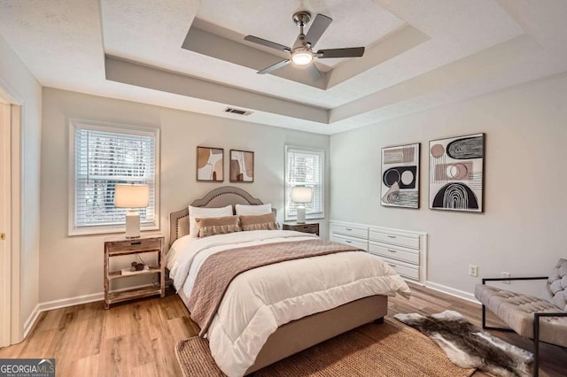 bedroom with light wood finished floors, multiple windows, and a raised ceiling