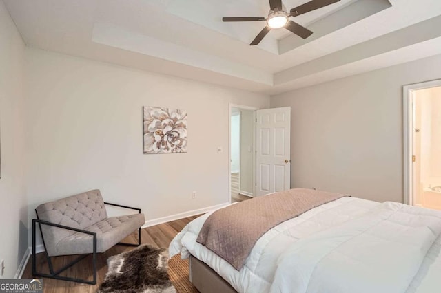 bedroom with a raised ceiling, ensuite bathroom, baseboards, and wood finished floors