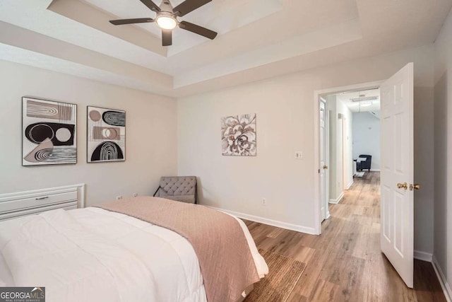 bedroom with light wood-style floors, a raised ceiling, and baseboards