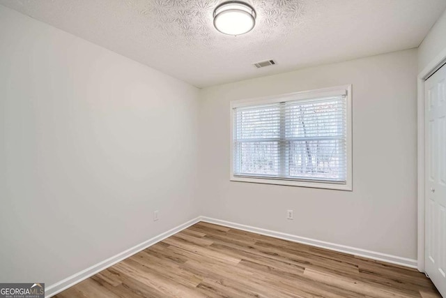 unfurnished bedroom featuring a textured ceiling, wood finished floors, visible vents, baseboards, and a closet