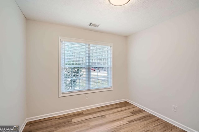 unfurnished room featuring light wood-style floors, visible vents, baseboards, and a textured ceiling