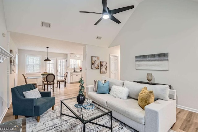 living room featuring light wood finished floors, visible vents, baseboards, ceiling fan, and high vaulted ceiling