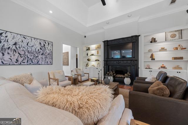 living room featuring visible vents, built in features, ceiling fan, ornamental molding, and a fireplace