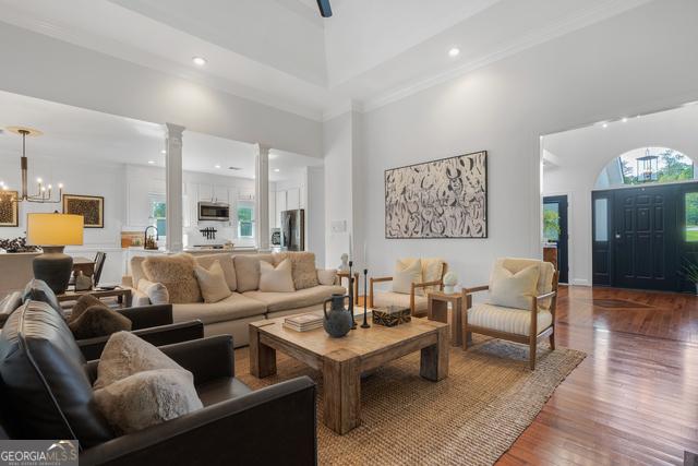 living room with a towering ceiling, wood finished floors, an inviting chandelier, ornate columns, and recessed lighting