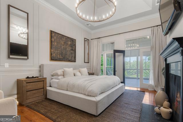 bedroom with wood finished floors, access to exterior, an inviting chandelier, crown molding, and a decorative wall