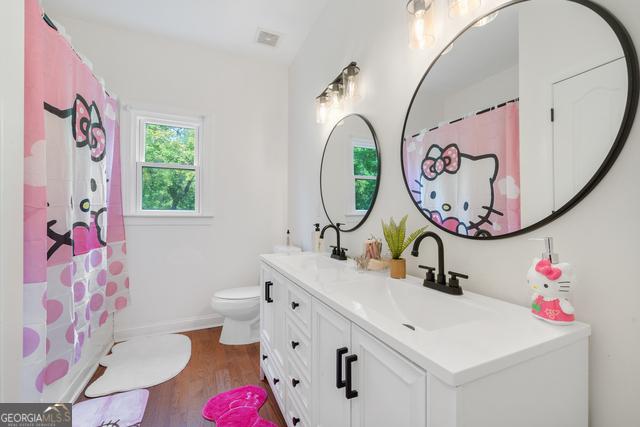 bathroom with toilet, wood finished floors, visible vents, a sink, and double vanity