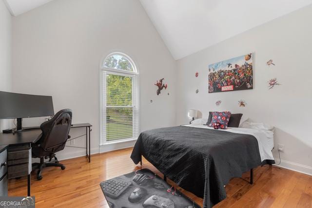 bedroom with light wood-style floors, high vaulted ceiling, and baseboards