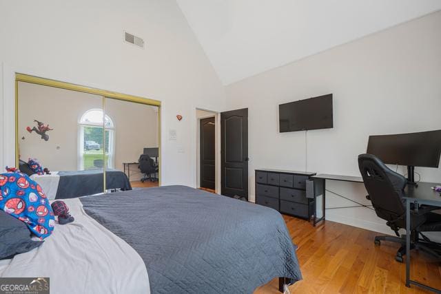 bedroom featuring high vaulted ceiling, a closet, visible vents, and wood finished floors