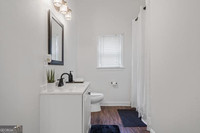 bathroom with curtained shower, toilet, vanity, wood finished floors, and baseboards