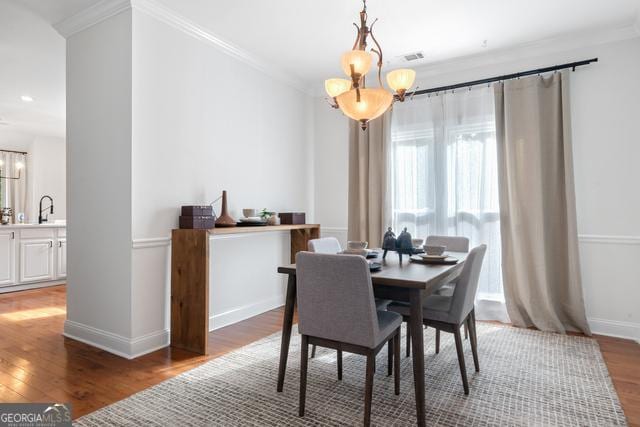 dining room with ornamental molding, a notable chandelier, and wood finished floors