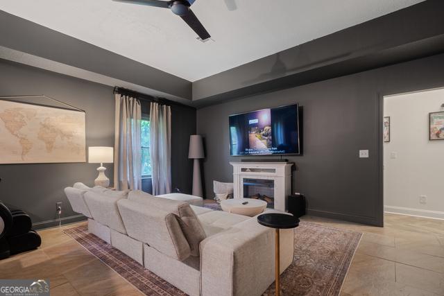 living room featuring a glass covered fireplace, ceiling fan, and baseboards