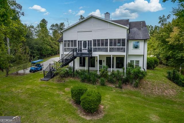 back of house with a sunroom, a chimney, stairway, and a lawn