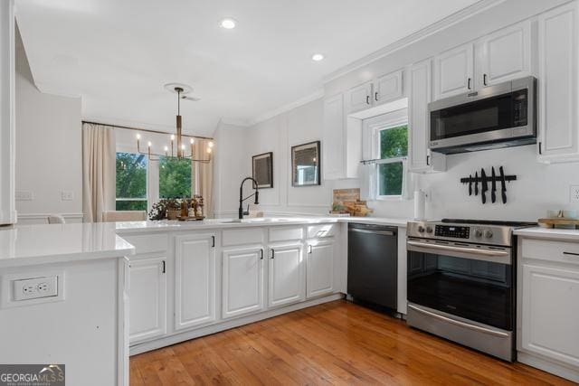 kitchen featuring plenty of natural light, white cabinets, appliances with stainless steel finishes, ornamental molding, and a sink