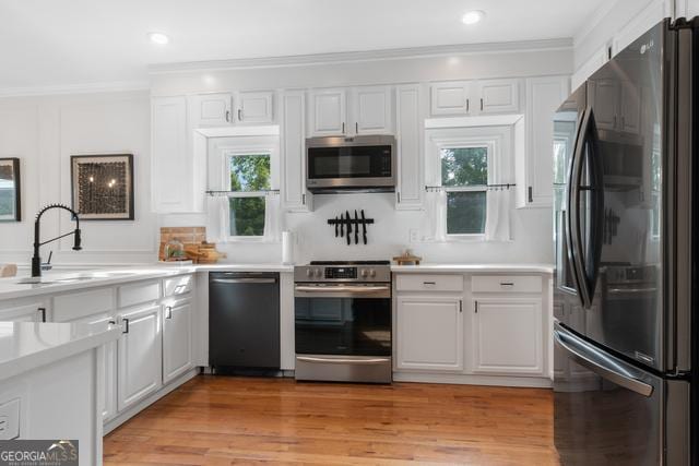 kitchen with white cabinets, appliances with stainless steel finishes, light countertops, crown molding, and light wood-style floors