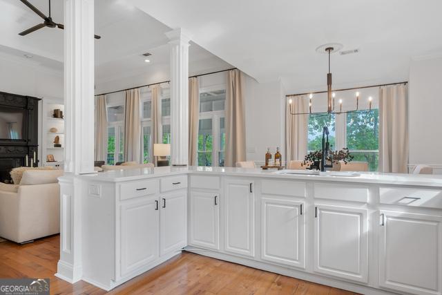 kitchen featuring ceiling fan with notable chandelier, a sink, white cabinets, light wood-style floors, and hanging light fixtures