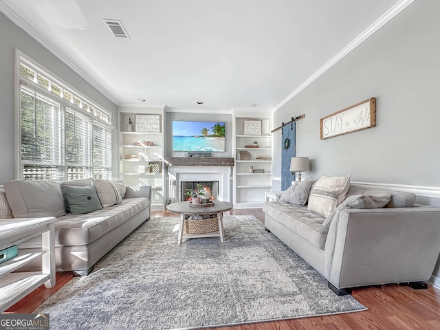 living area with visible vents, a barn door, ornamental molding, wood finished floors, and a warm lit fireplace