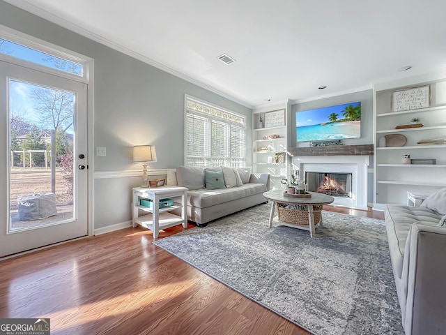 living area with ornamental molding, visible vents, plenty of natural light, and wood finished floors