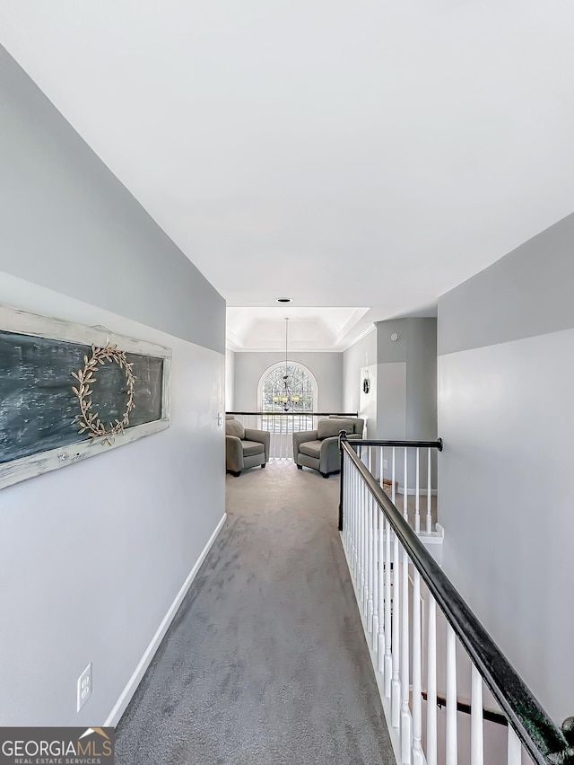 corridor featuring a tray ceiling, carpet flooring, an upstairs landing, a chandelier, and baseboards