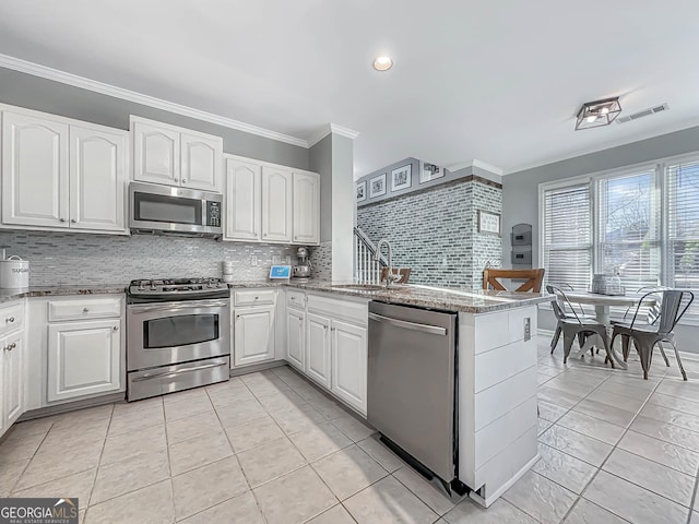 kitchen featuring stainless steel appliances, a sink, white cabinetry, light stone countertops, and crown molding