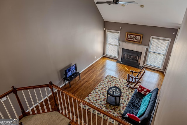 living room featuring baseboards, a ceiling fan, a fireplace with flush hearth, wood finished floors, and vaulted ceiling