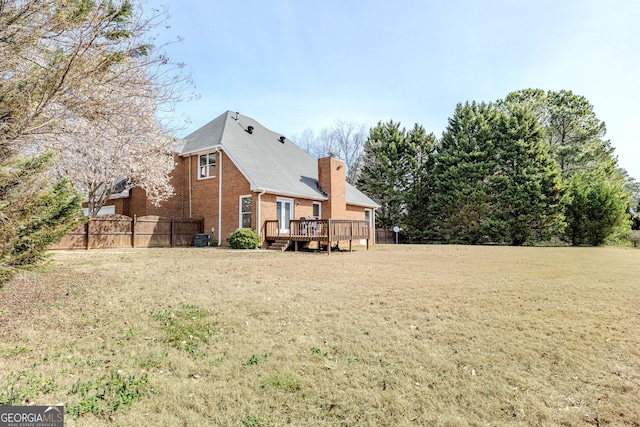 rear view of property with a lawn, a chimney, fence, a deck, and brick siding