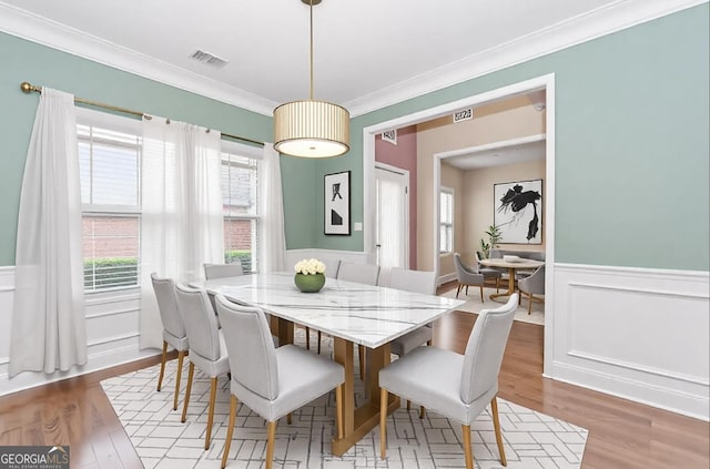 dining space with ornamental molding, visible vents, wood finished floors, and a healthy amount of sunlight