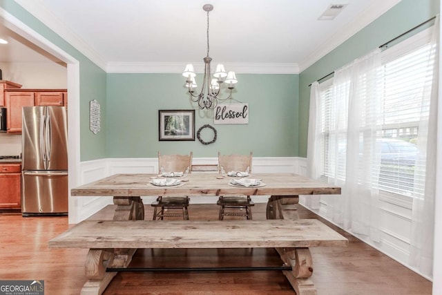 dining room featuring ornamental molding, wainscoting, visible vents, and light wood finished floors